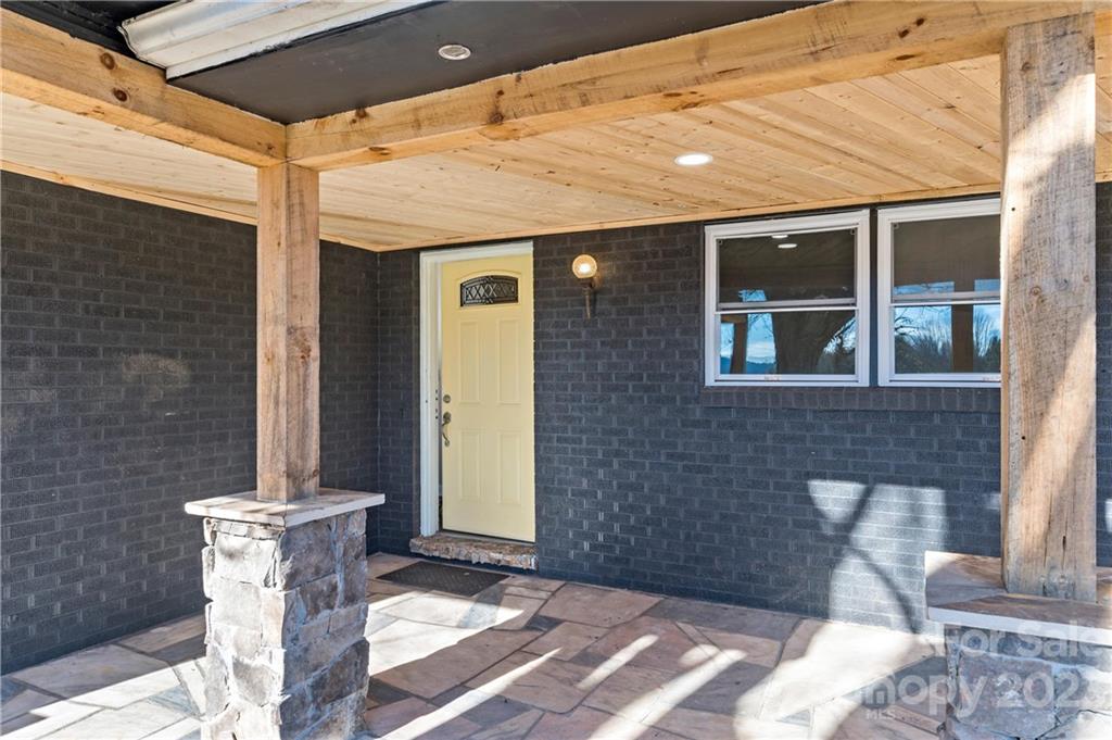 Covered brick entry porch with a yellow door, timber posts, and a wood-plank ceiling.