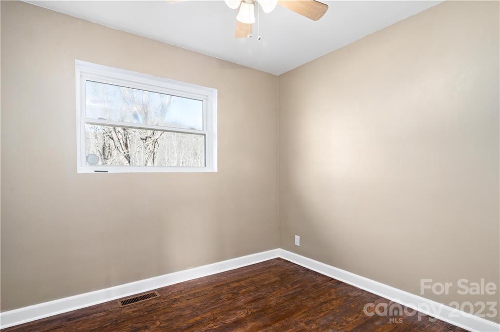 Empty room with dark hardwood floors, beige walls, and a window overlooking leafless trees.
