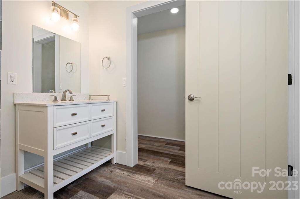 Bathroom with a white double-sink vanity and an open doorway to a wood-look-floored hall.