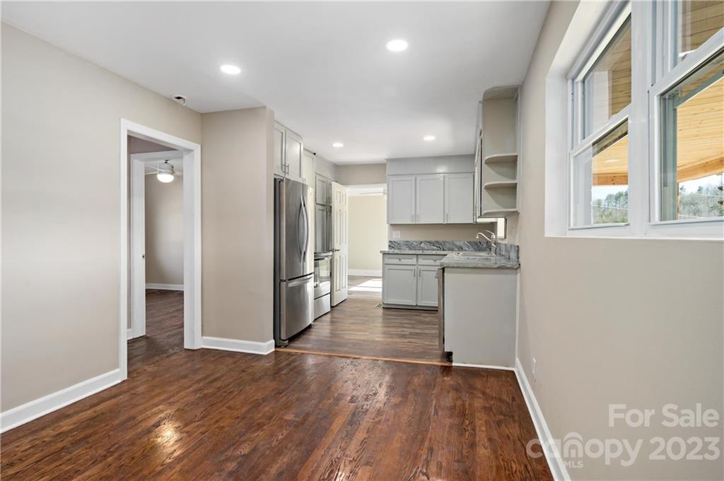 Vacant kitchen with white cabinetry, stainless steel appliances, granite counters, and dark wood floors.