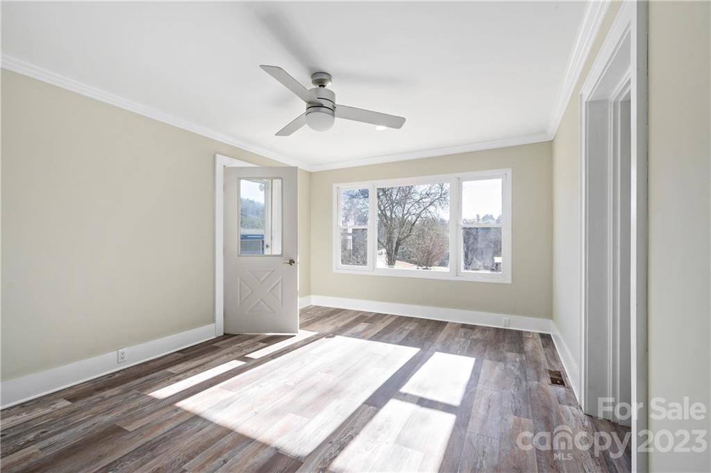 Vacant room with wide-plank flooring, ceiling fan, and windows overlooking winter trees.