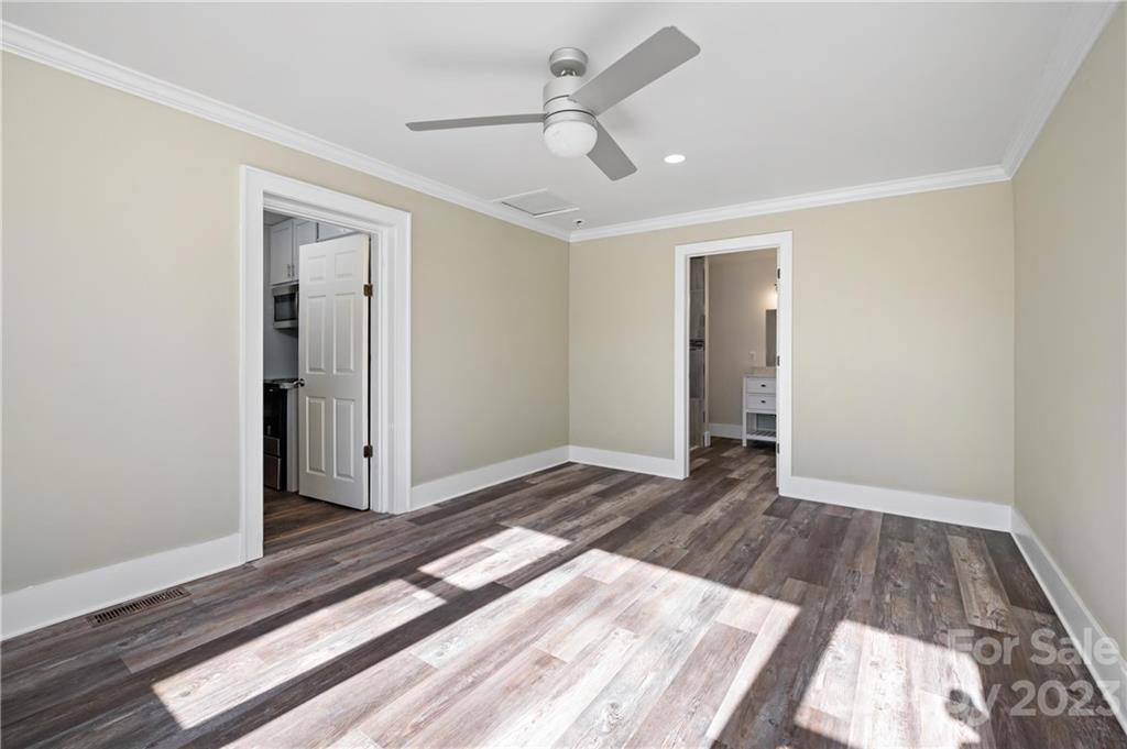 Vacant room with plank flooring, ceiling fan, and doorways to adjoining spaces.