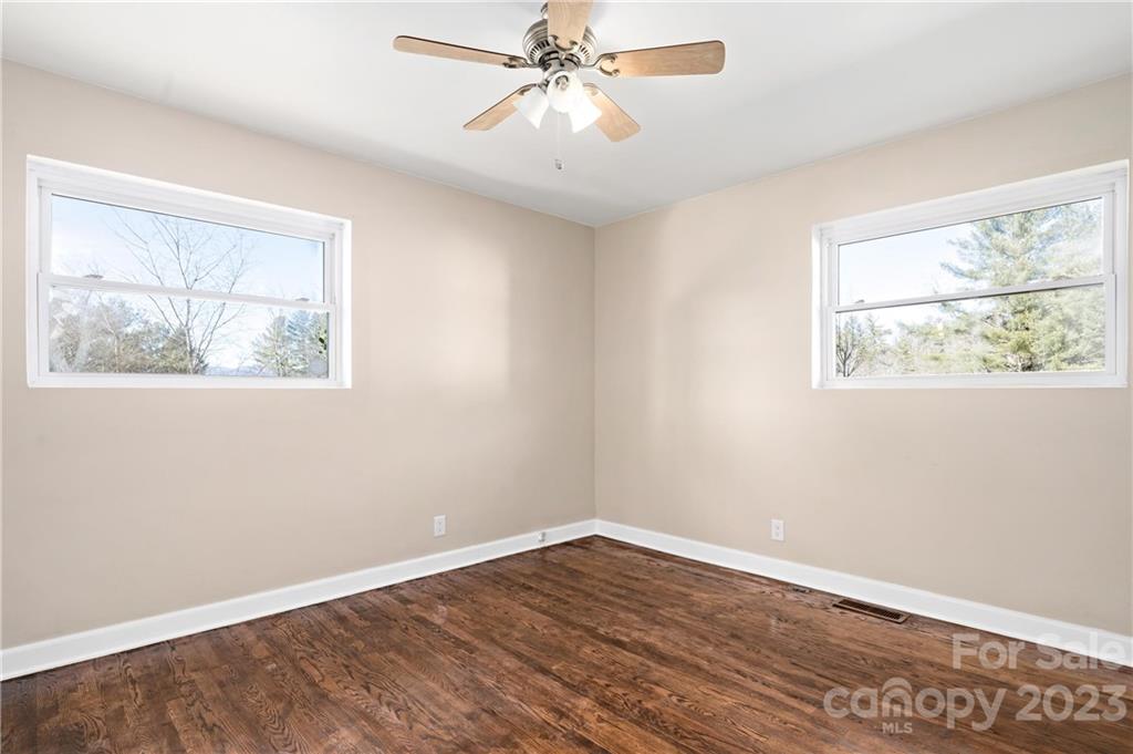 Empty bedroom with dark hardwood floors, two windows, and a ceiling fan.