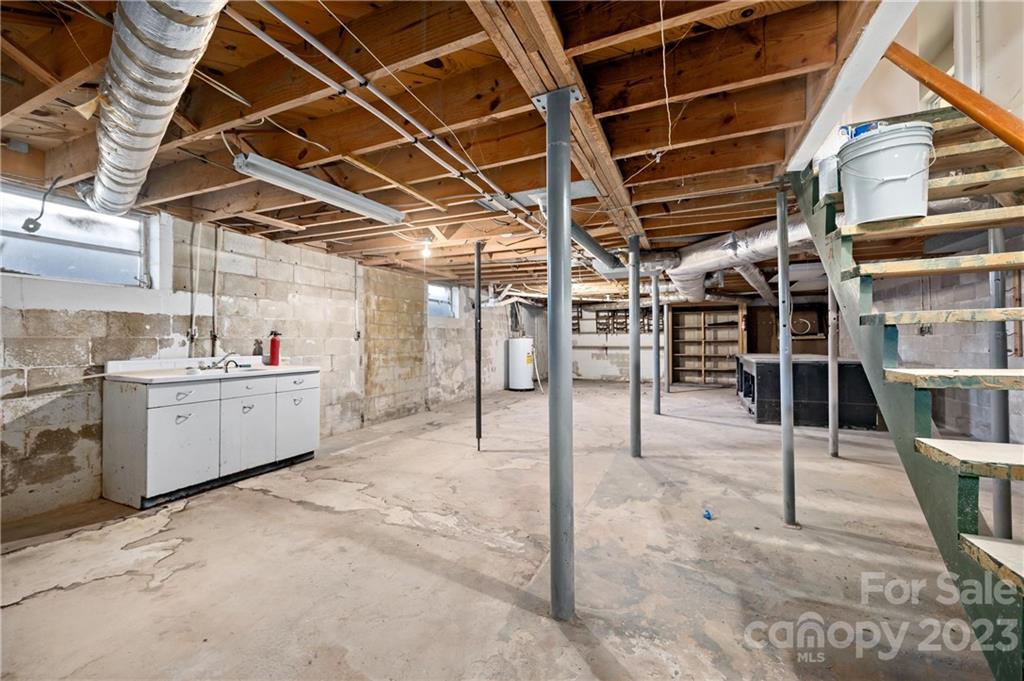 Unfinished basement with exposed joists, concrete block walls, support posts, and a utility sink.