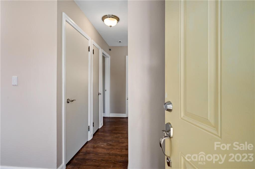Entry door opens onto a vacant hallway with dark wood flooring and several white doors.