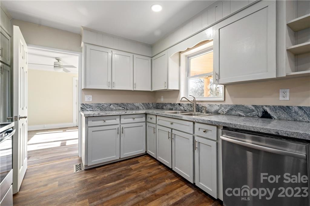 Kitchen with white cabinets, gray granite countertops, stainless-steel dishwasher, and dark wood flooring.