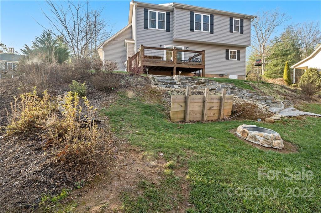 Rear of a gray two-story house with a raised deck above a sloping, stone-walled yard.