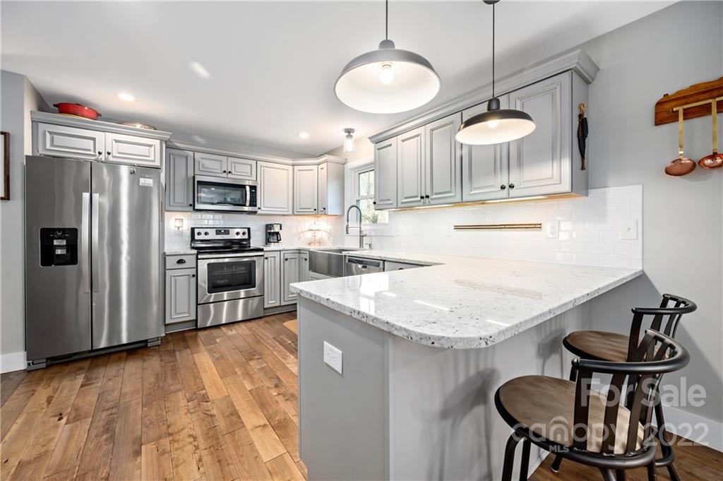 Kitchen with gray cabinets, stainless steel appliances, white stone peninsula, and warm wood flooring.