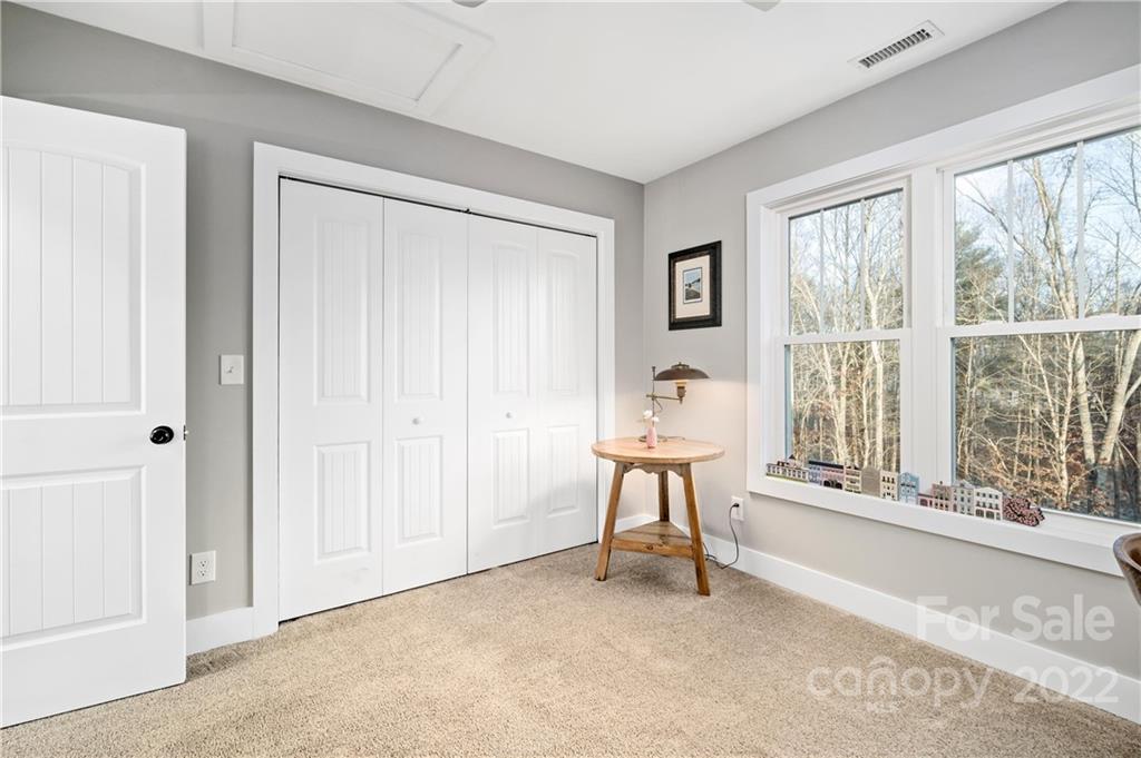 Carpeted bedroom with white paneled closet doors and large windows overlooking trees.