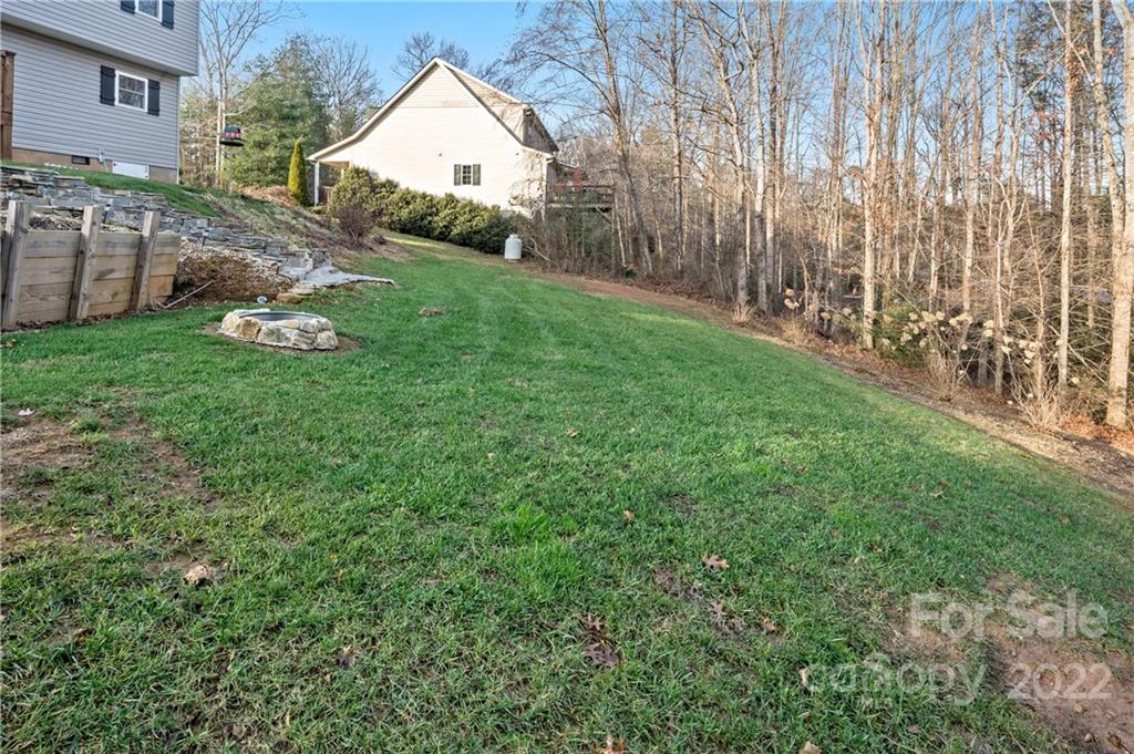 Sloping grassy backyard bordered by a stone retaining wall and leafless woods.