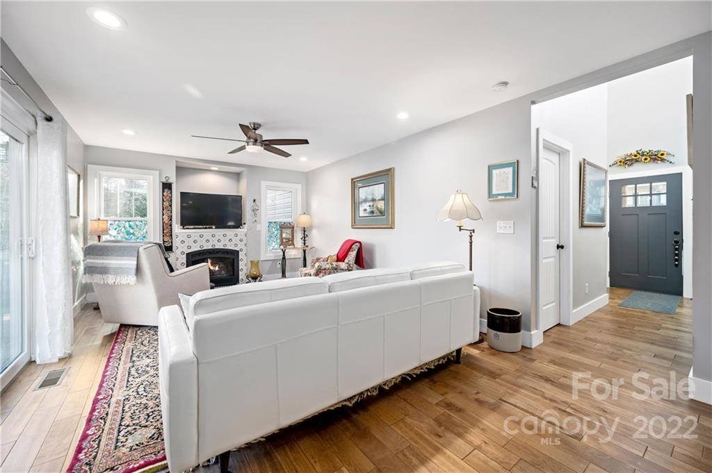 Furnished living room with white sofas, a patterned rug, and a fireplace beneath the television.