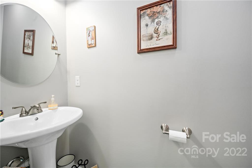 Bathroom with a white pedestal sink, large round mirror, and framed wall art.