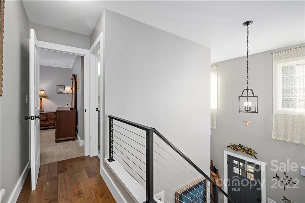 Upstairs landing with wood floors, black metal railing, and a view into the bright two-story foyer.