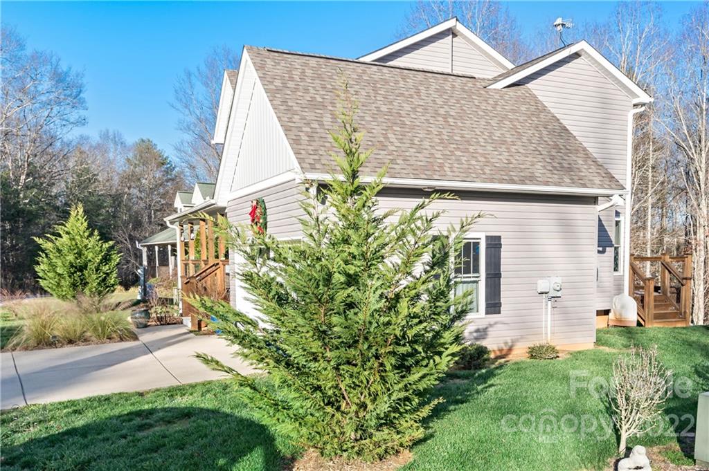 Light-sided home with a steep shingle roof, wooden porch, and concrete driveway.