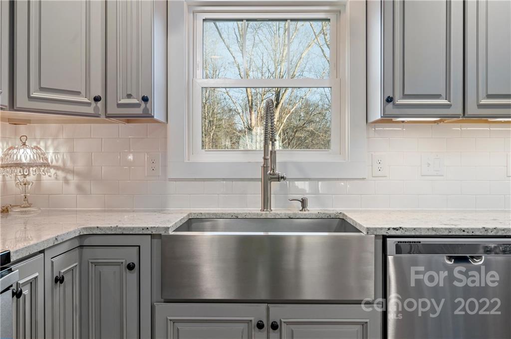 Kitchen with a large stainless steel farmhouse sink, gray cabinets, and a window overlooking bare trees.