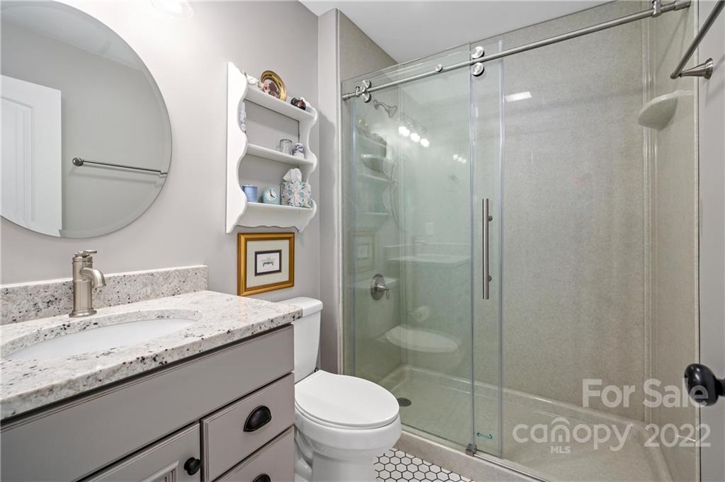 Bathroom with a speckled granite vanity, round mirror, and glass-enclosed shower.