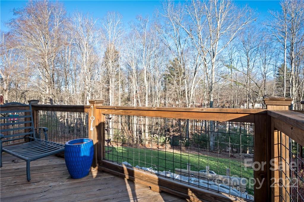 Wooden deck overlooking a lawn and leafless woods, with a lounge chair and blue planter.