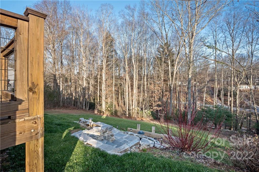 Stone patio in a grassy backyard bordered by leafless trees, with a wooden deck at left.