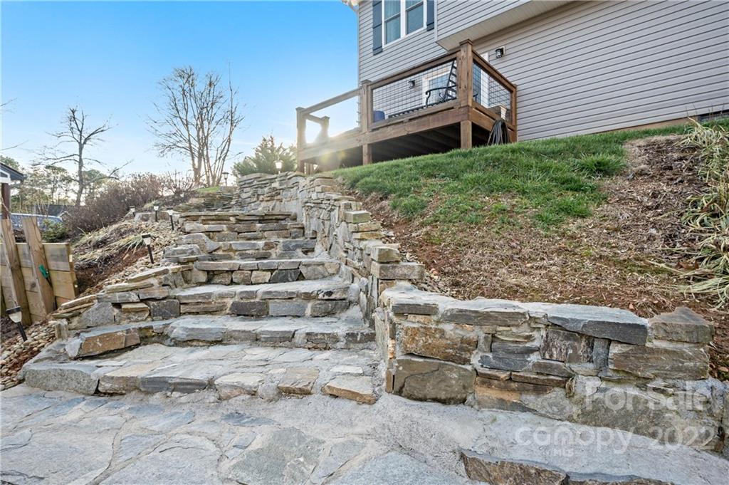 Stone steps and retaining walls lead up to a wooden deck beside a gray-sided home.