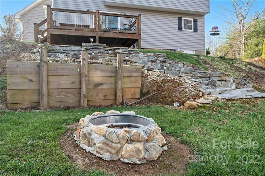 Backyard with a raised wooden deck, stone retaining walls and steps, and a circular stone fire pit.