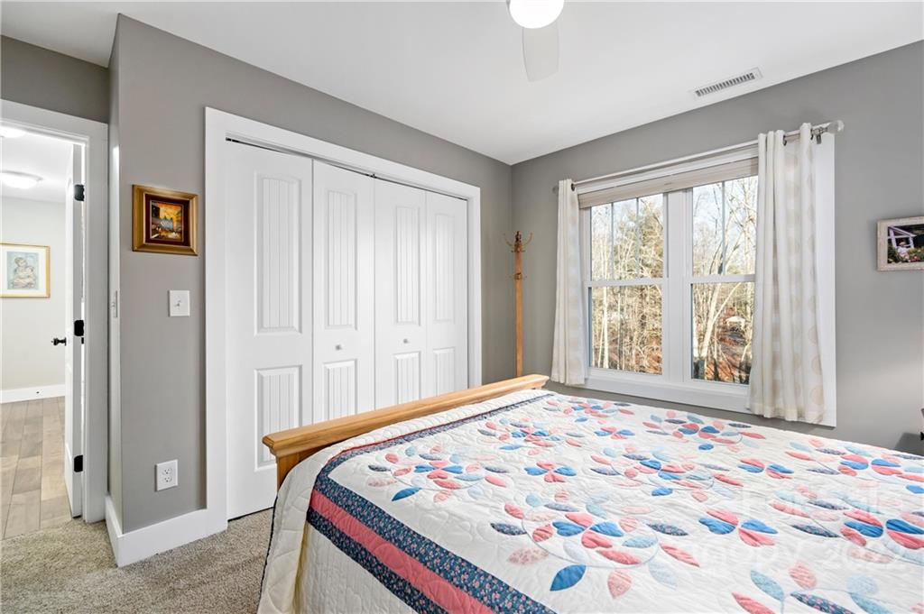 Bedroom with a colorful quilt, white closet doors, and a large window overlooking trees.