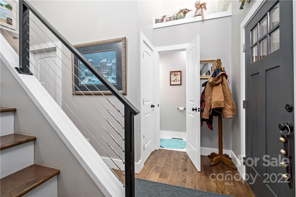 Entryway with a dark front door, cable-railed staircase, wood floors, and coats on a rack.