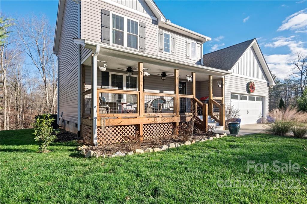 Two-story gray home with a covered wooden porch, seating, attached garage, and green lawn.