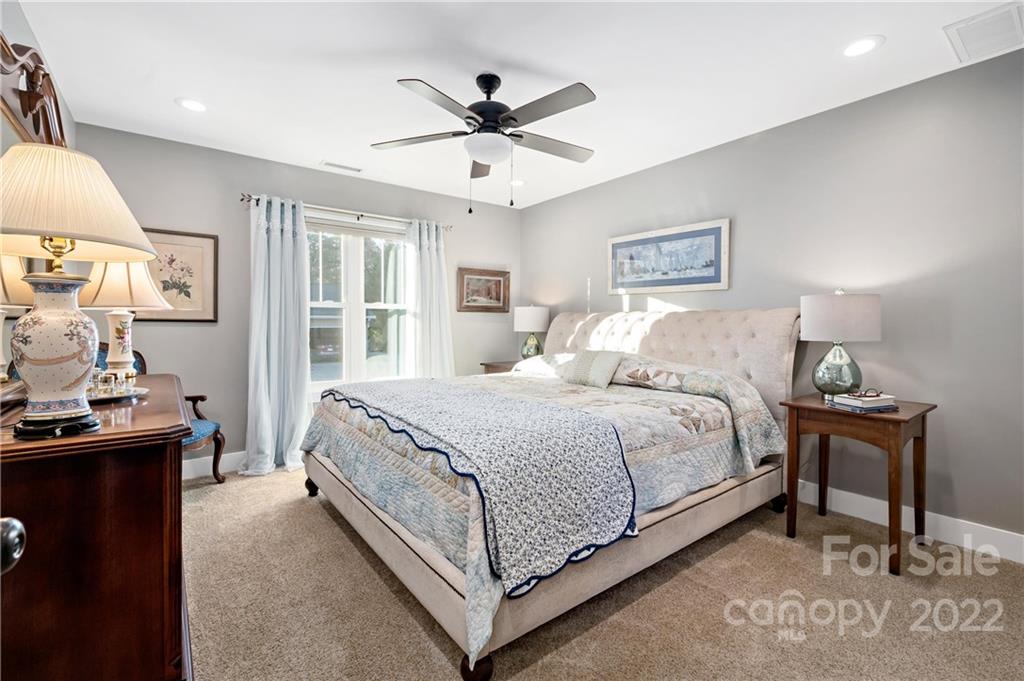 Bedroom with a tufted bed, pale blue curtains, and a ceiling fan.