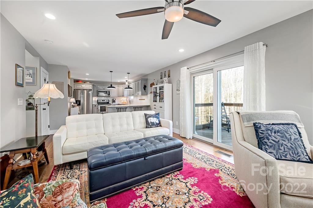 Furnished living room with a white sectional, pink patterned rug, and sliding doors to a wooded deck.