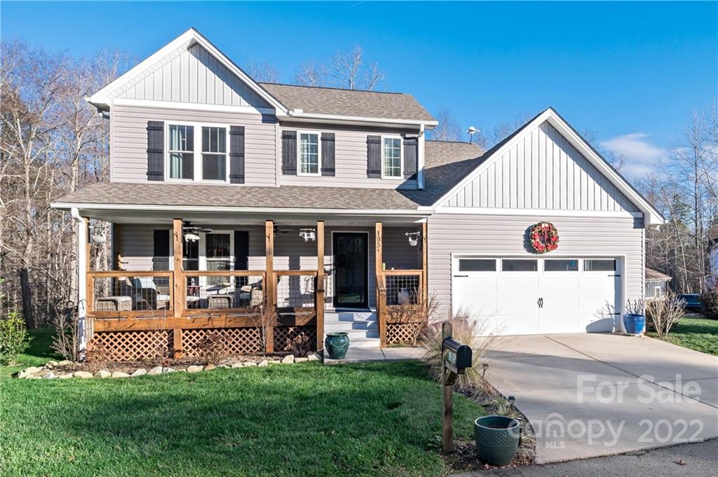 Two-story gray house with a covered wooden porch, attached garage, and holiday wreath.