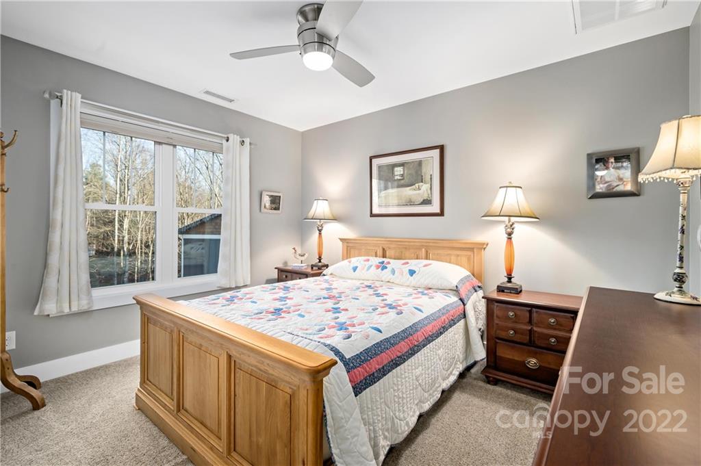 Bedroom with a wooden bed, colorful quilt, matching nightstands, and a large window overlooking trees.