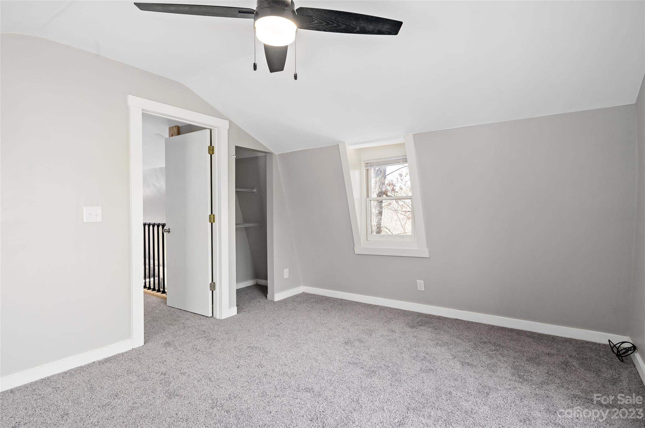 Empty upstairs bedroom with gray carpet, a sloped ceiling, and a small window.