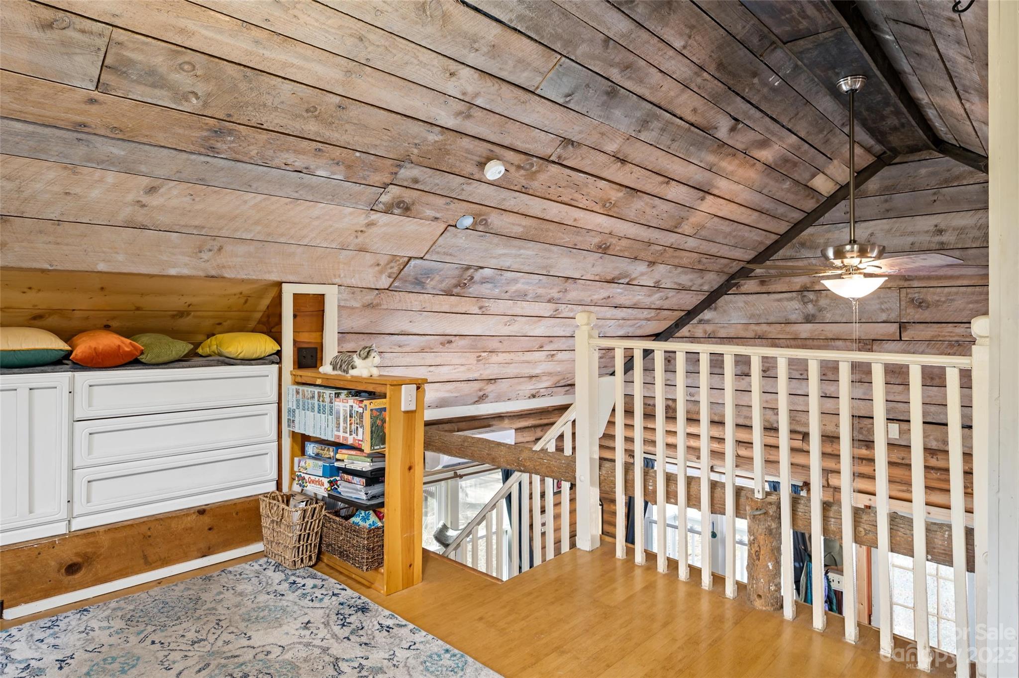 Furnished loft with rustic wood-plank walls, a built-in daybed, and railing around the stair opening.