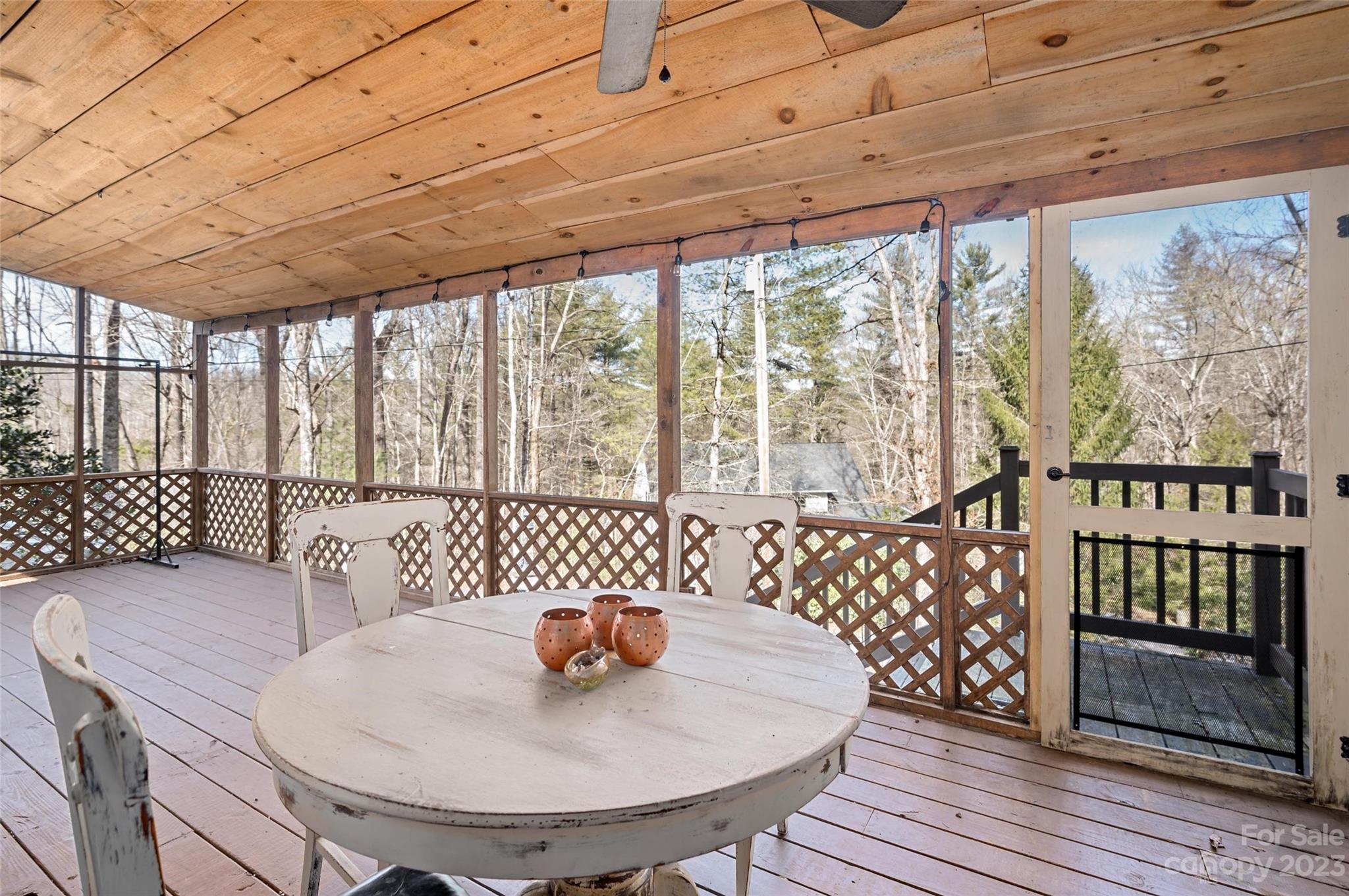 Covered wooden porch with a white round table, chairs, and views of leafless trees.