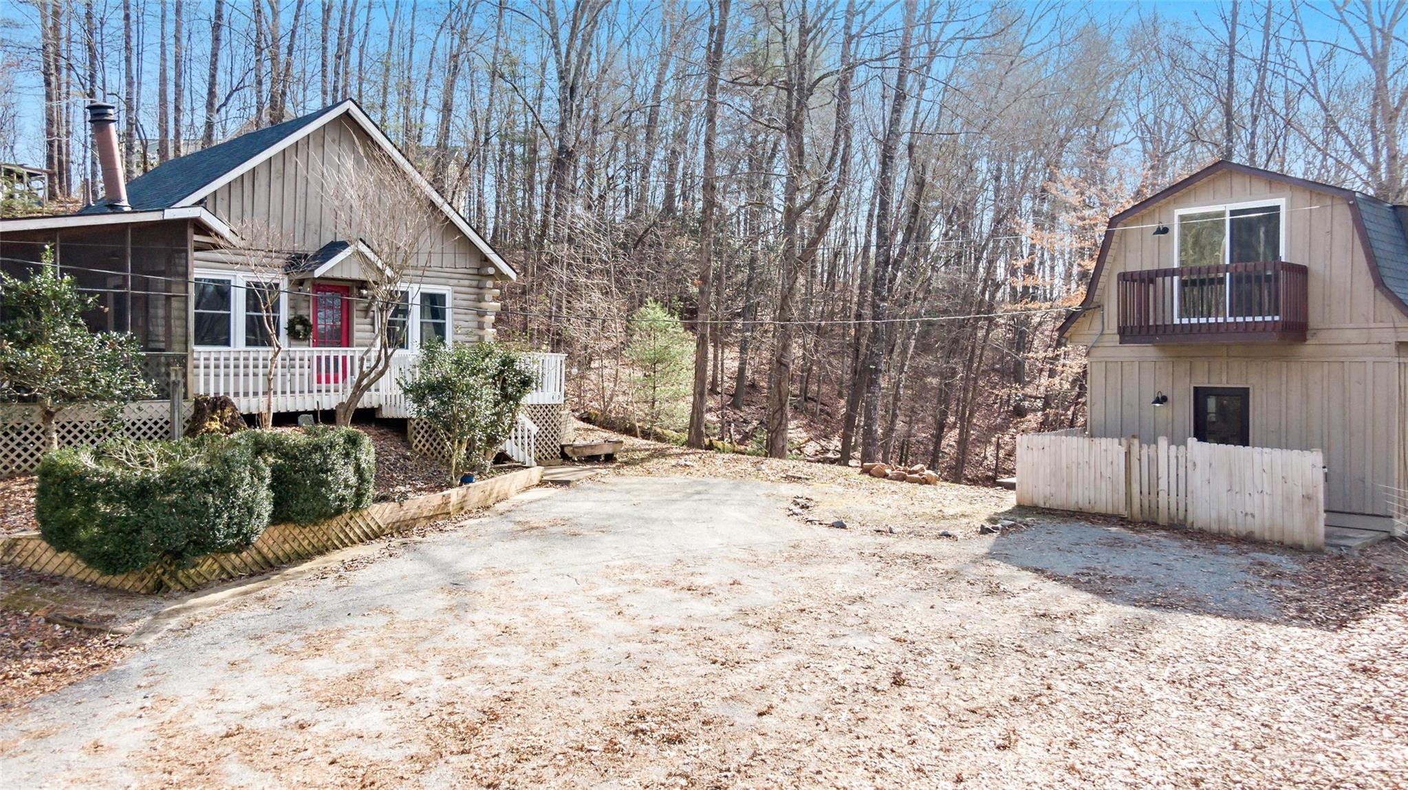 Two homes on a wooded lot, with a log cabin and red door beside a tan home with a balcony.