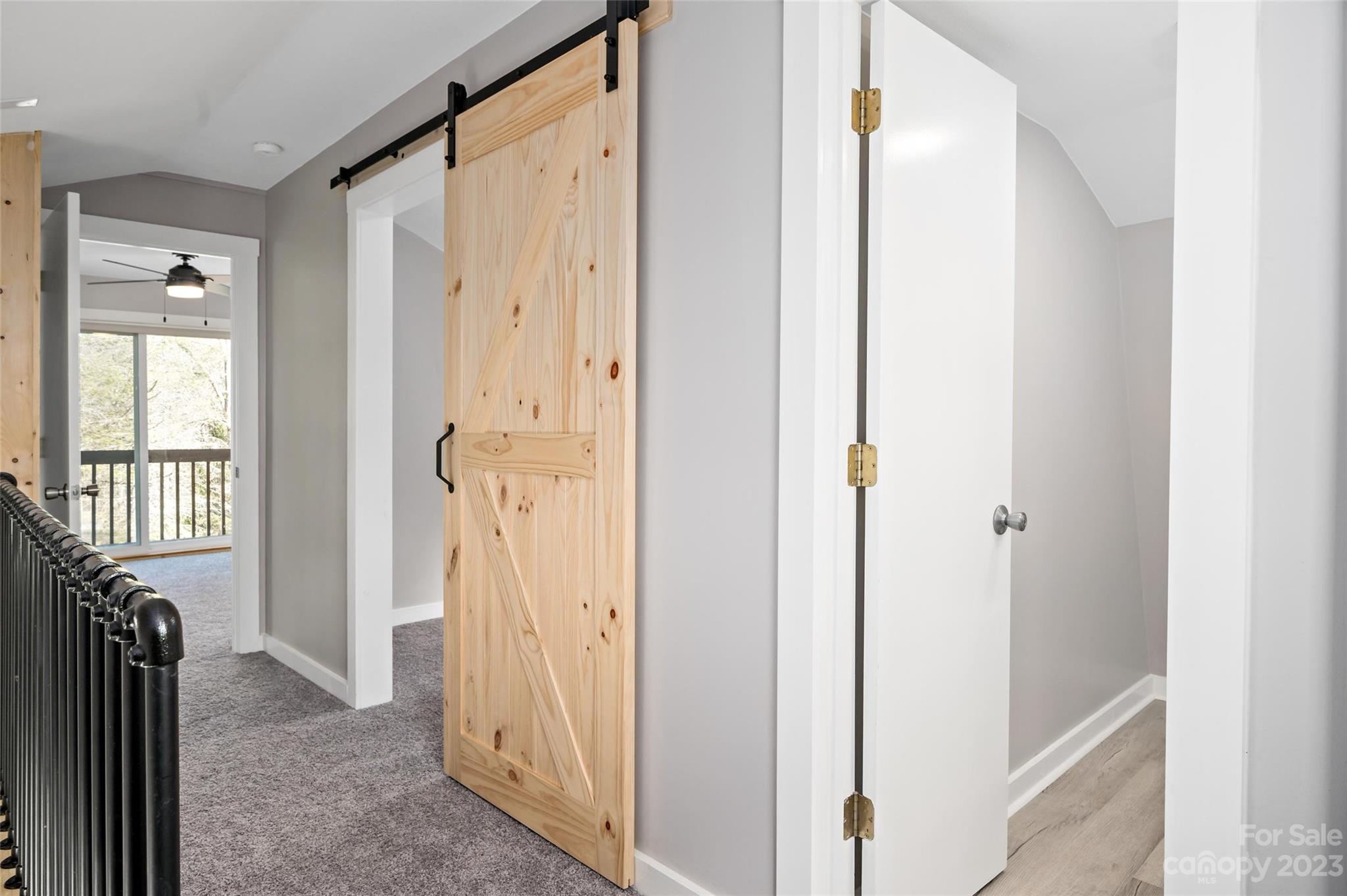Hallway with a natural wood barn door, black railing, and glass doors opening to a balcony.