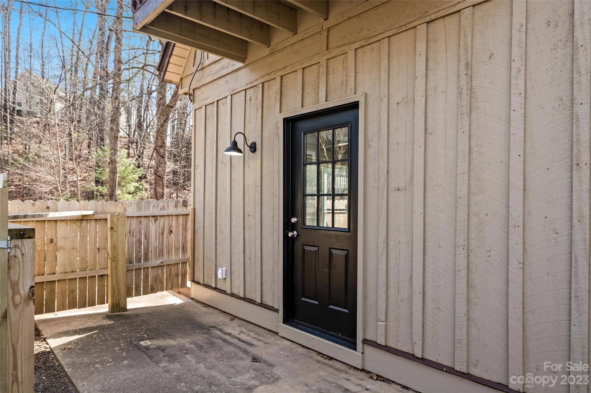 Exterior entry with a black divided-light door, covered concrete patio, and wooden privacy fence.
