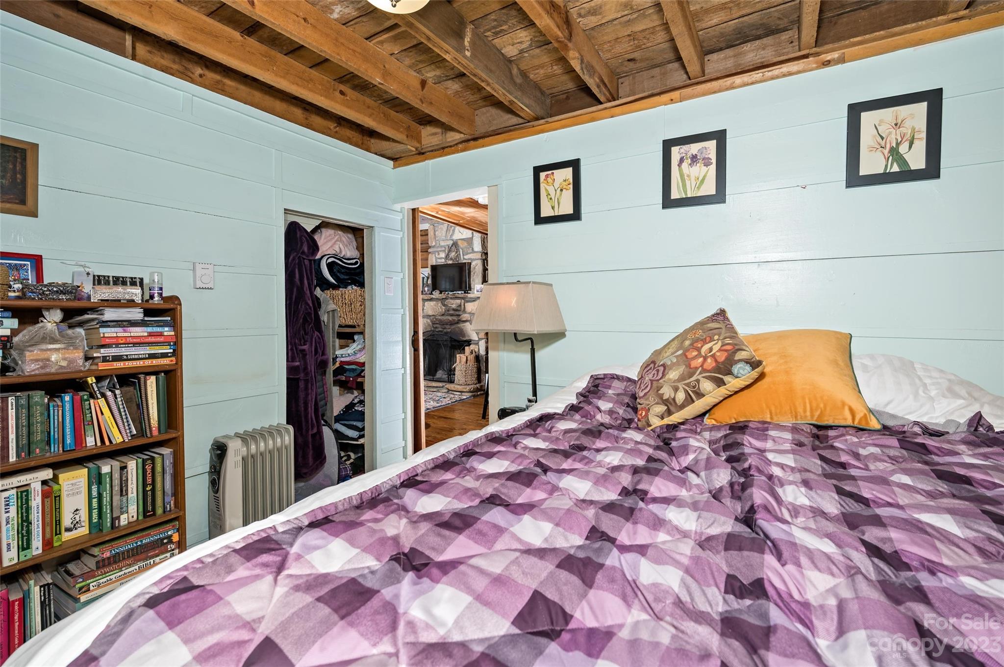 Bedroom with purple plaid bedding, pale blue paneled walls, and an exposed timber ceiling.