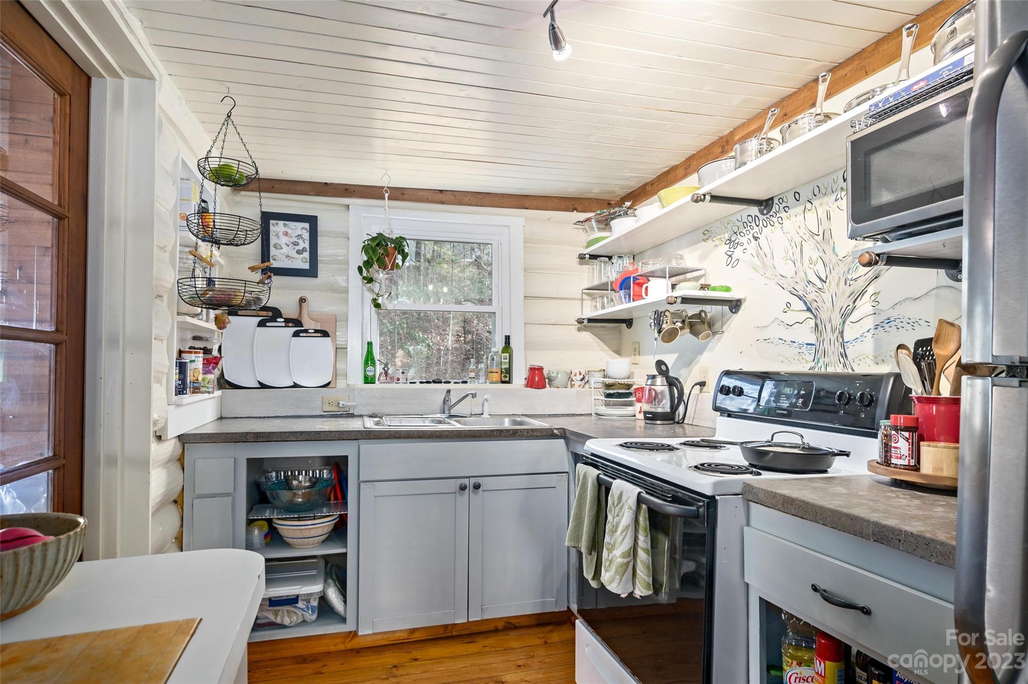 Kitchen with gray cabinets, open shelves, a tree mural backsplash, and an electric range.
