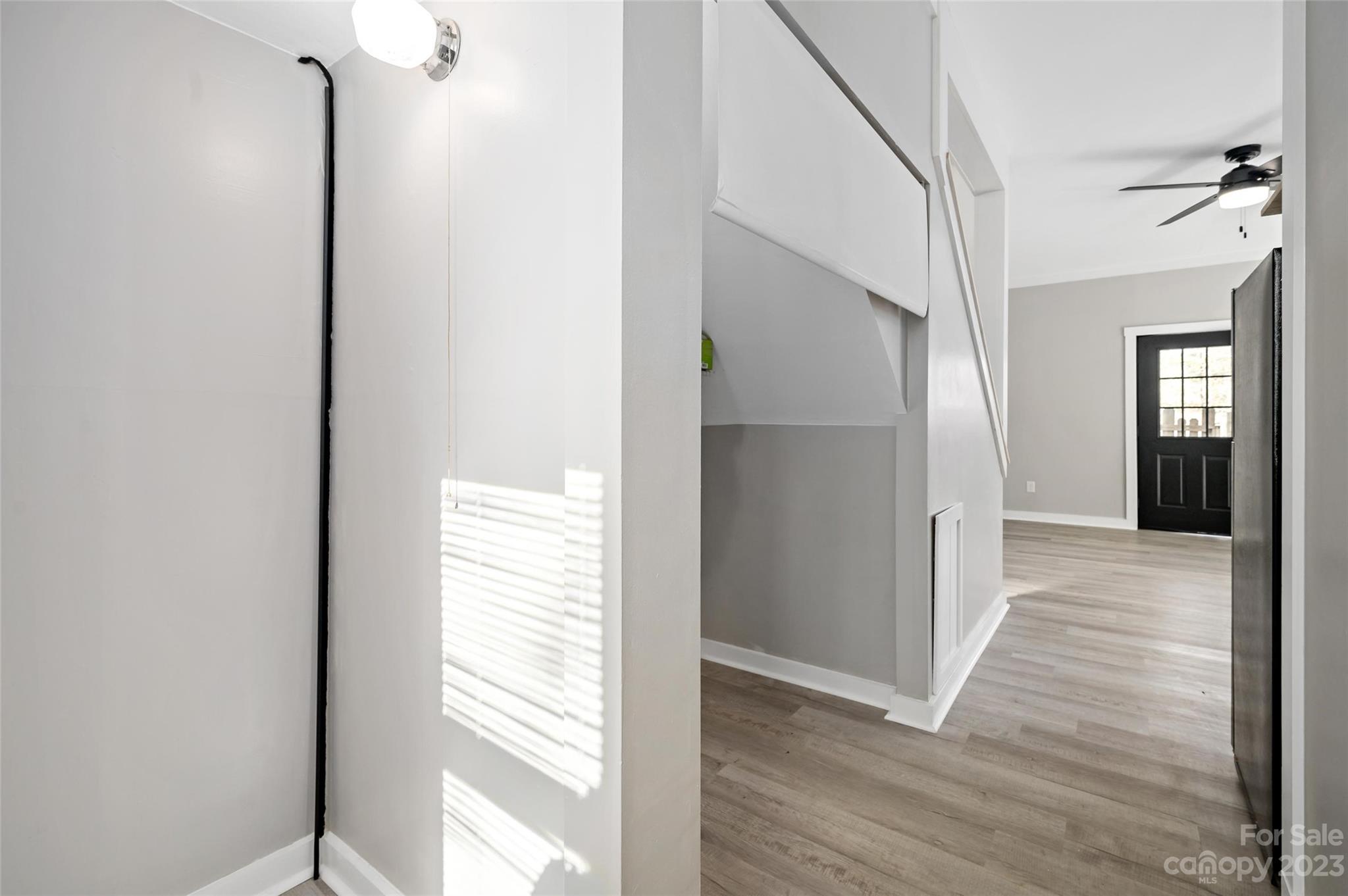 Empty hallway with light wood-look flooring, gray walls, and a black glass-paneled front door.