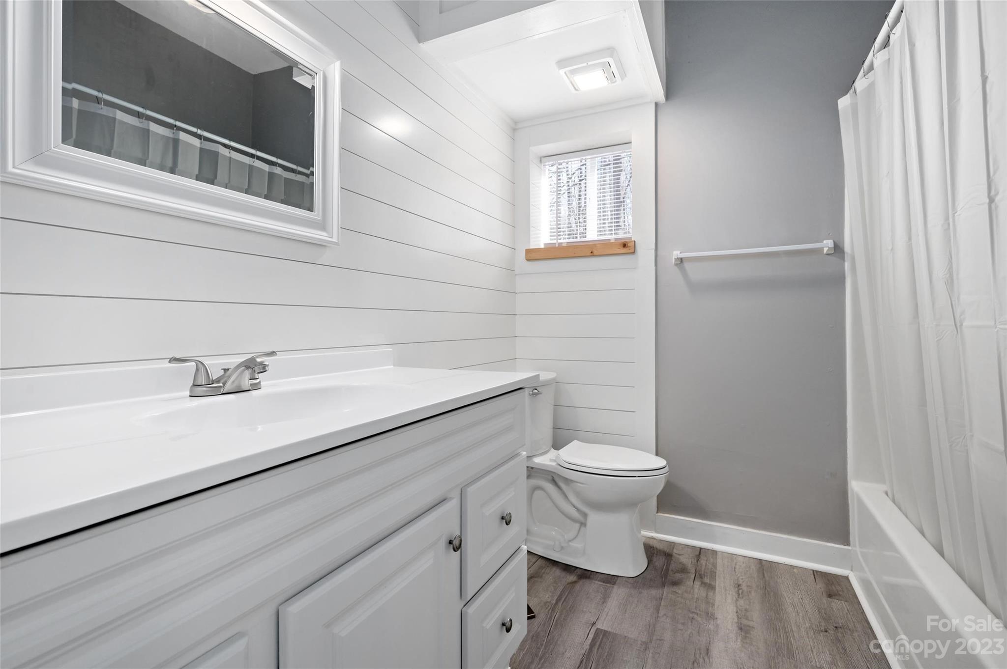 Bathroom with a white vanity, gray walls, horizontal paneling, and gray-brown plank flooring.