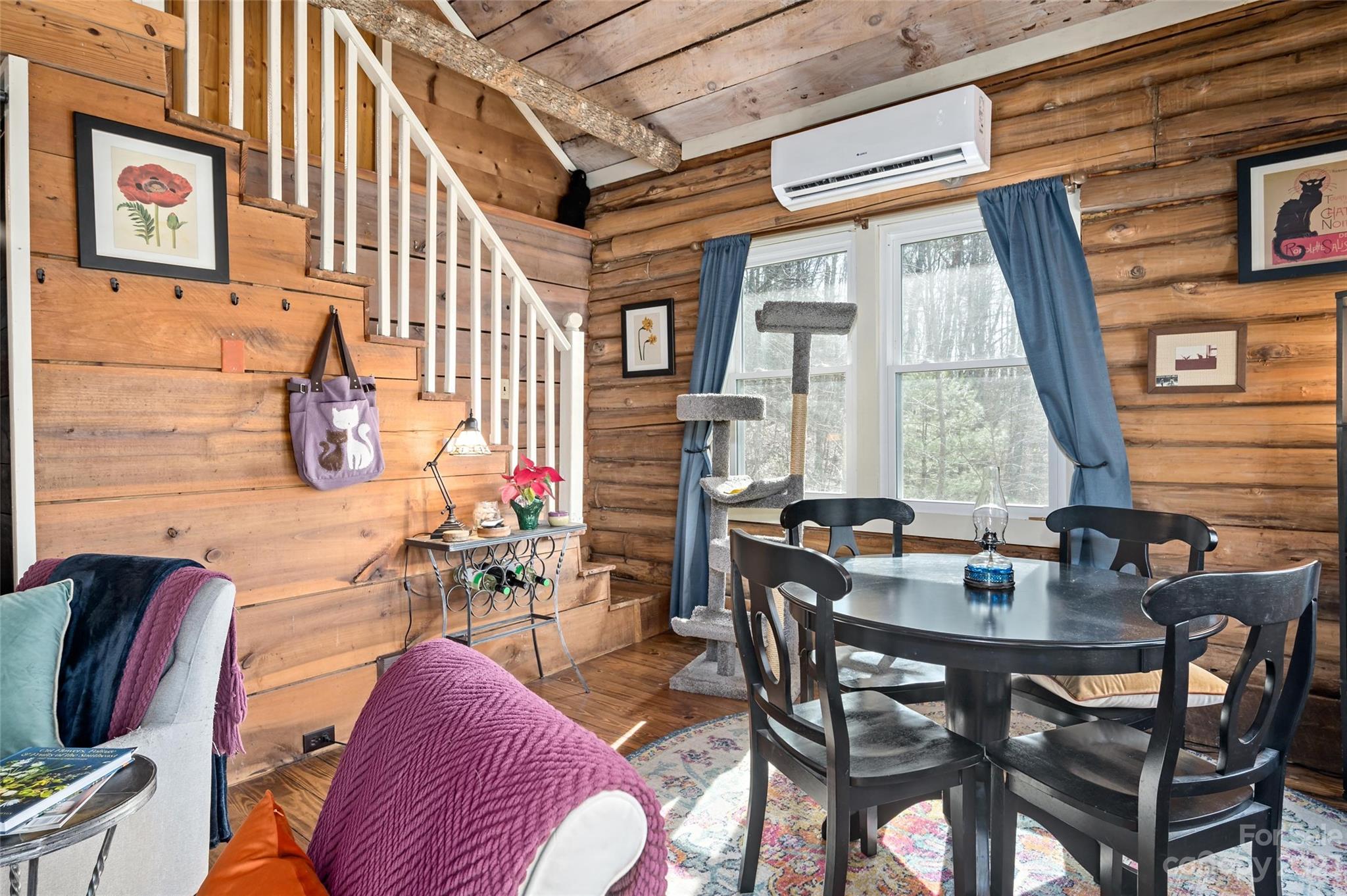 Log cabin dining and living area with exposed wood walls, staircase, and large curtained windows.