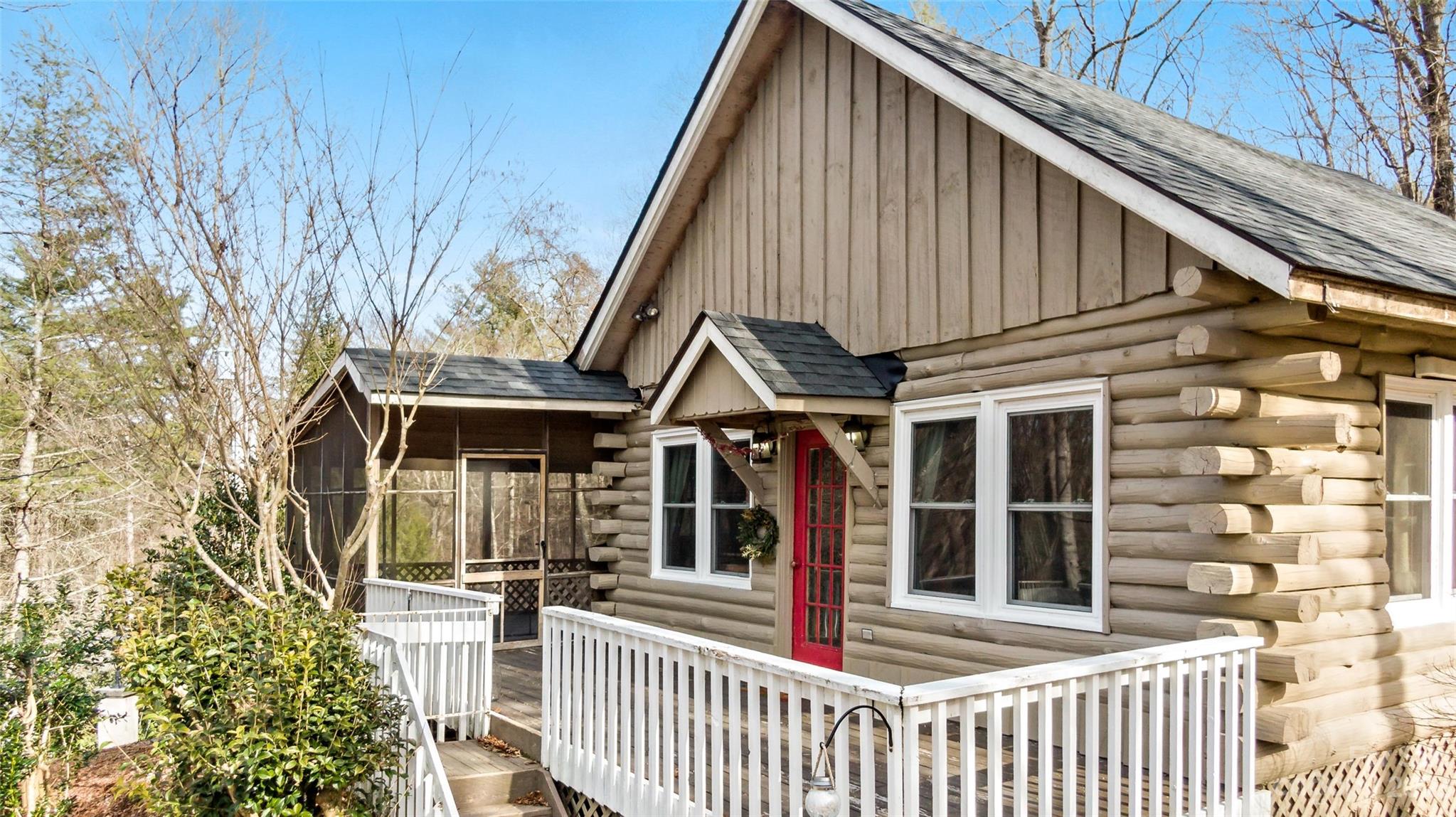Log cabin with a red front door, white-railed deck, and screened porch.