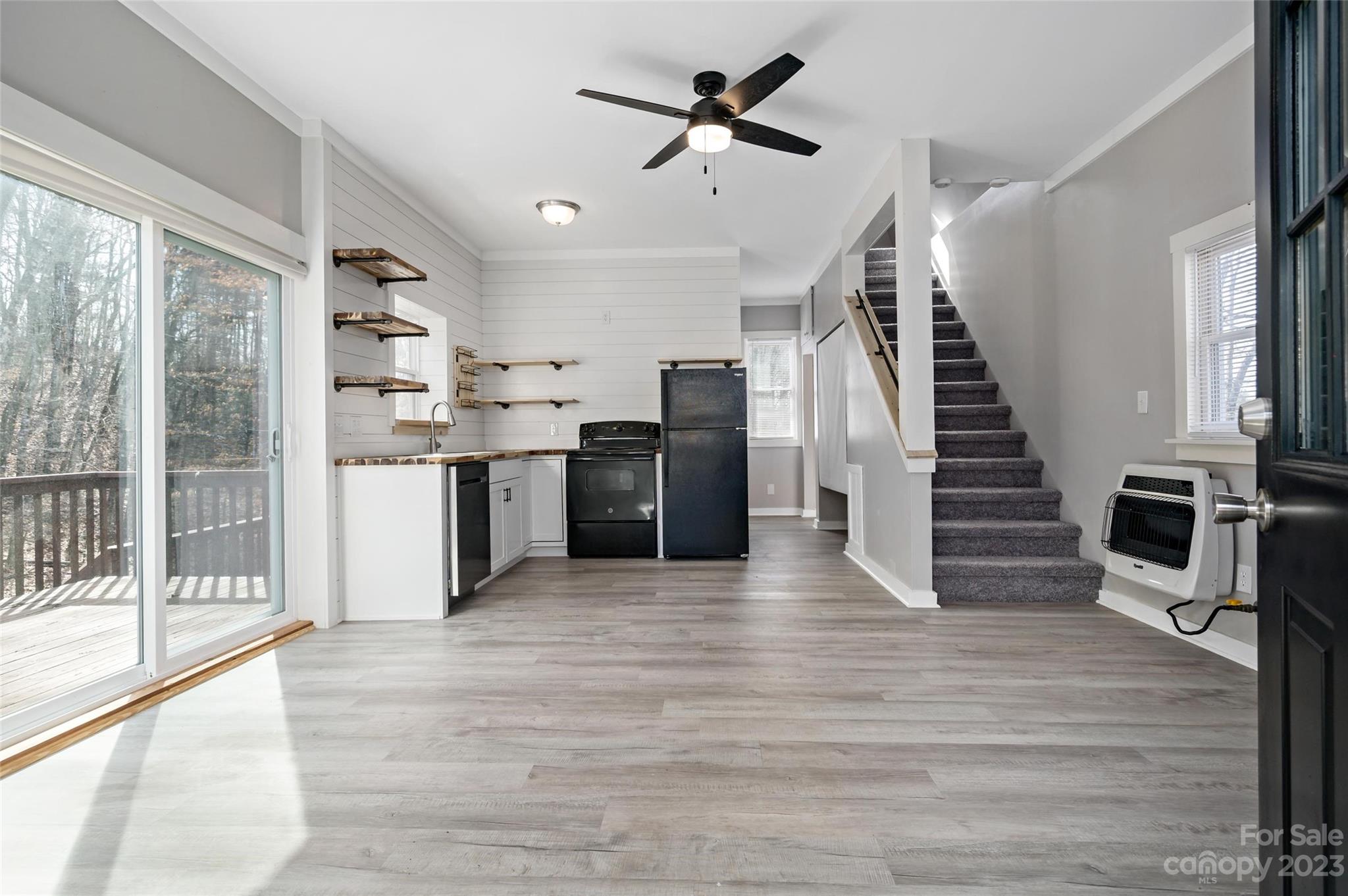 Open-plan kitchen and living area with black appliances, sliding glass doors, and carpeted stairs.