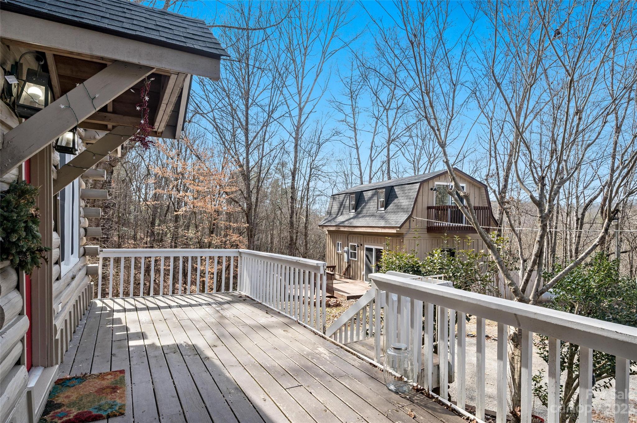 Wooden deck with white railings overlooking a second cabin among leafless trees.