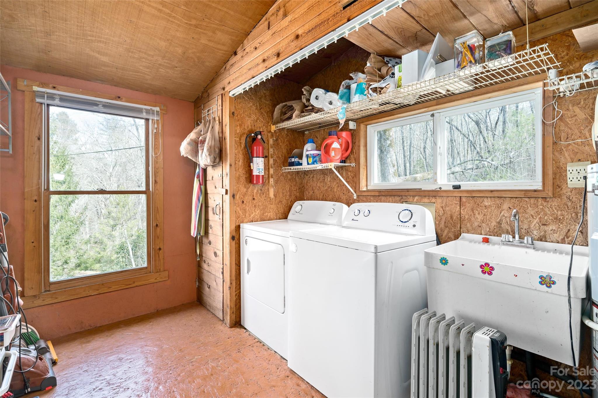 Laundry room with washer, dryer, utility sink, and large windows overlooking trees.
