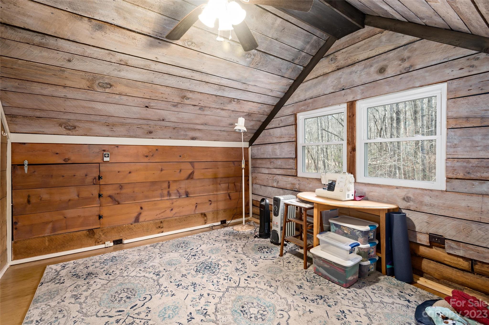 Attic craft room with a sewing machine beneath windows, rustic plank walls, and a patterned rug.