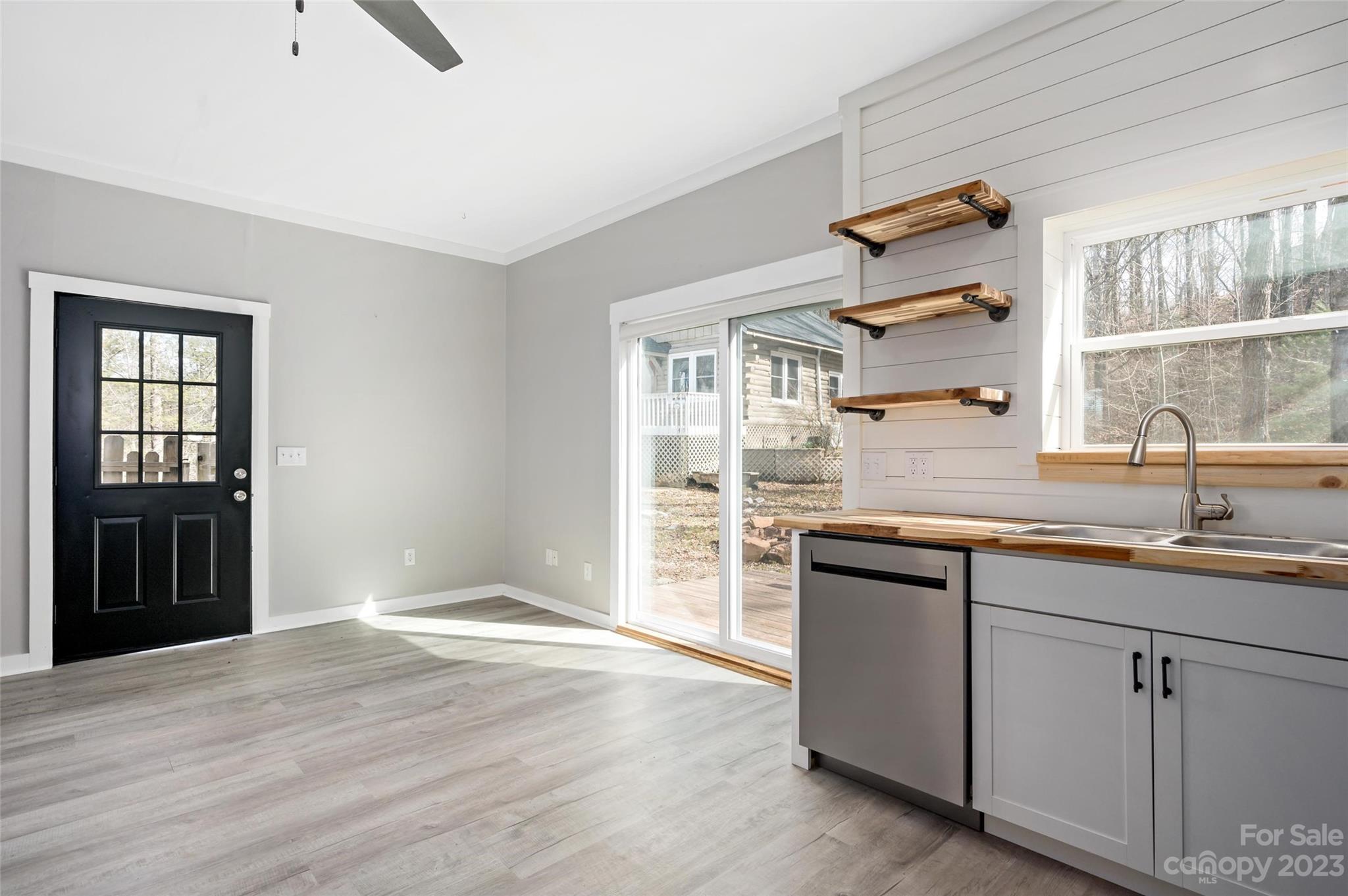 Vacant kitchen with gray cabinets, wood countertops and shelves, and a sliding glass door beside the black entry door.