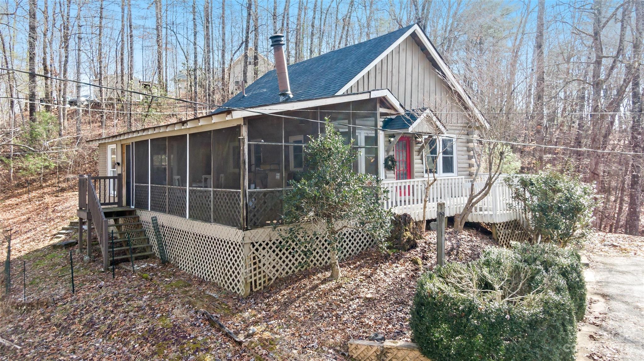 Rustic cabin with a screened porch and red front door among leafless trees.