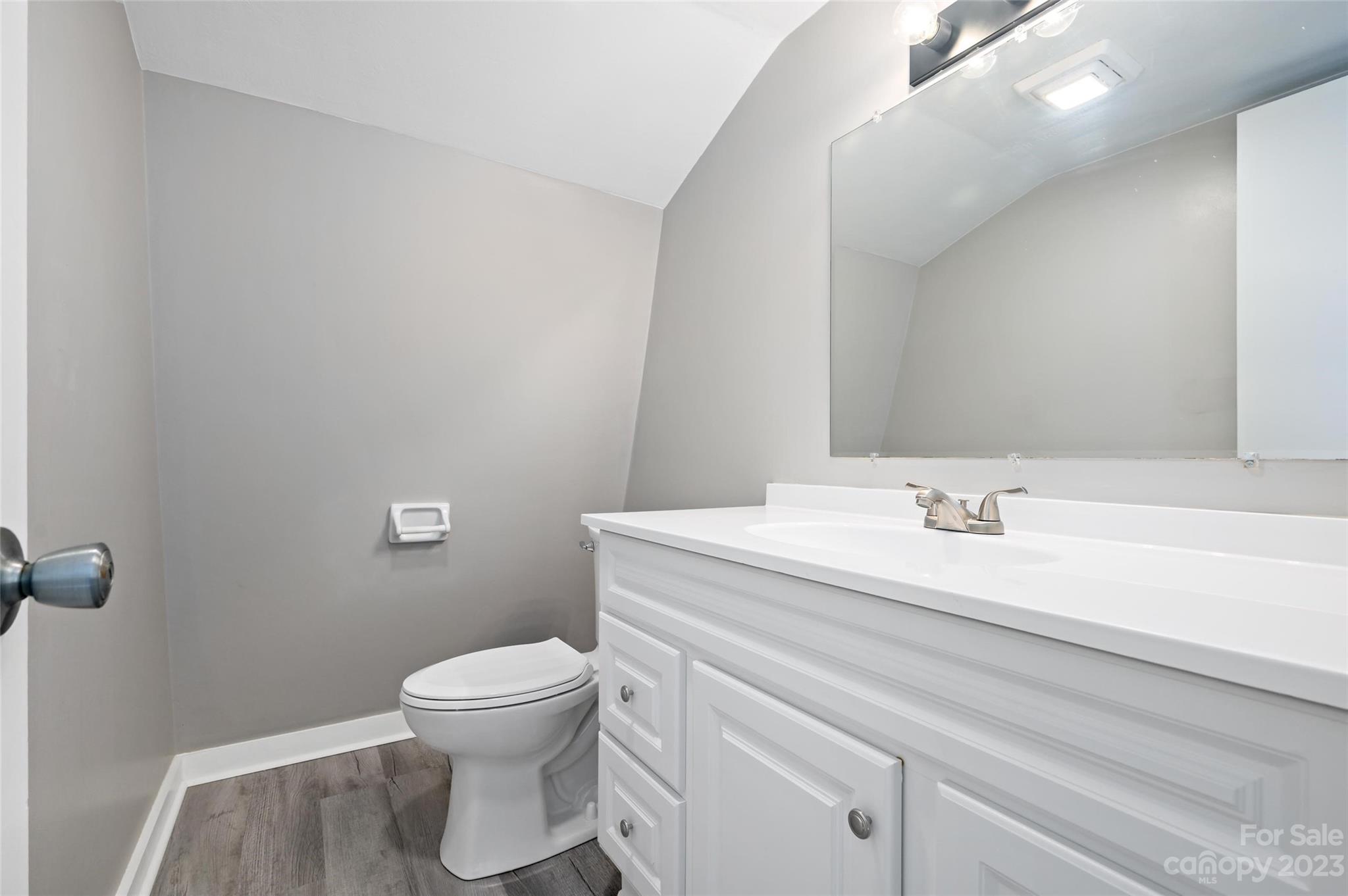Bathroom with a white vanity and large mirror beside a toilet under a sloped ceiling.